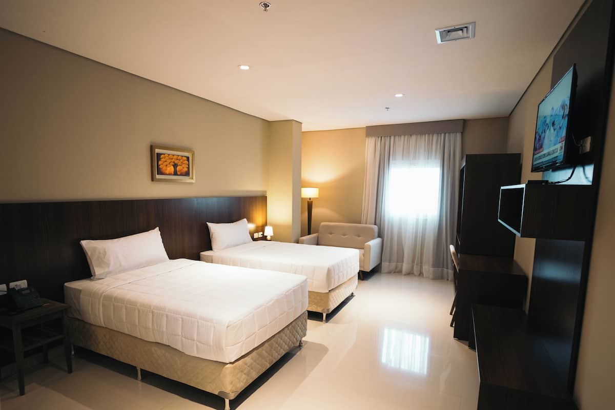 A hotel room with two beds, a desk, a chair, a TV, and a window with curtains.