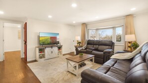 Ein modernes Wohnzimmer mit einer Ledersofa, einem Holztisch und einem Flachbildfernseher, der an einem weißen Schrank befestigt ist.