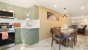 Eine moderne Küche mit Einbau-Mikrowelle, Backofen und Spüle. Es gibt einen Essbereich mit Tisch und Stühlen sowie ein Wohnzimmer mit Sofa und Liegesessel.