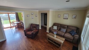 A spacious living room with a brown leather sofa, a wooden coffee table, and a dining area with a table and chairs. - Cardinal Cottage - 2 bedroom cozy home (Muncie)