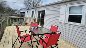 A deck with a table and chairs, a wooden fence, and a house with white siding and a window. - Cardinal Cottage - 2 bedroom cozy home (Muncie)