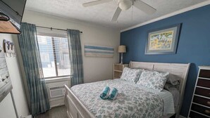 A bedroom with a bed, a ceiling fan, a window with curtains, a radiator, and a dresser. - Toes In The Sand (North Topsail Beach)