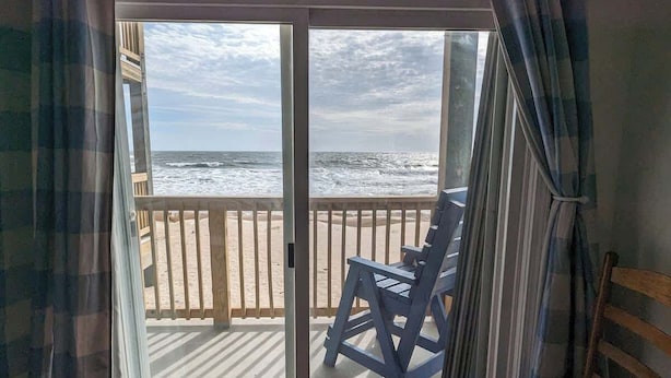 A room with a view of the ocean through a sliding glass door, a wooden deck, and a blue chair. - Toes In The Sand (North Topsail Beach)
