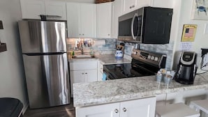 A kitchen with white cabinets, stainless steel appliances, a marble countertop, and a coffee maker. - Toes In The Sand (North Topsail Beach)