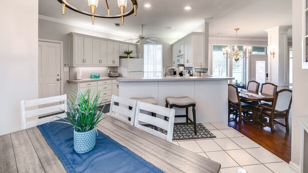 Une cuisine moderne avec des meubles blancs, un îlot central et un coin repas comprenant une table et des chaises en bois.