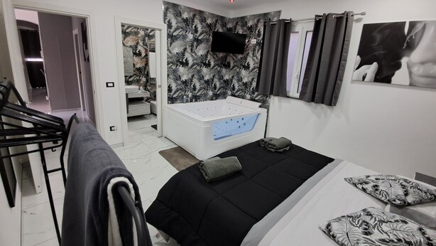 Ein modernes Schlafzimmer mit einem großen Bett, einem separaten Badezimmer mit Badewanne und einem an der Wand befestigten Fernseher.