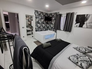Een moderne slaapkamer met een groot bed, een aparte badkamer met een badkuip, en een aan de muur bevestigde televisie.