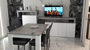 Eine moderne Küche mit integriertem Fernseher, eine Essecke mit Tisch und Stühlen sowie ein Schlafzimmer mit Bett und Handtüchern.