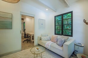 A living room with a sofa, a glass coffee table, and a large window with a view of trees.