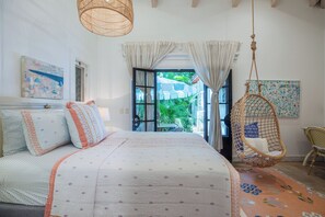 A bedroom with a bed, a hanging chair, and a view of the outdoors.