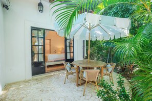A patio with a round wooden table and wicker chairs, surrounded by lush greenery and a white umbrella. - Designer 3 bdr Spanish Style Villa with 25m Lap Pool in the Heart of Guiones. (Nosara)