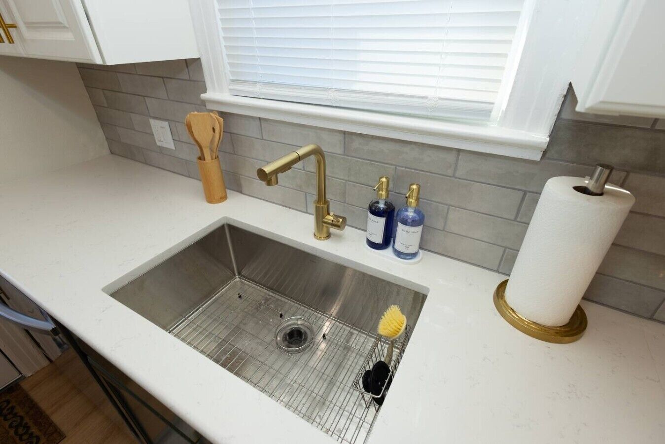Une cuisine avec un évier en acier inoxydable, une fenêtre avec des stores et un rouleau de papier toilette posé sur le comptoir.