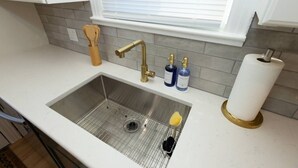 Una cocina con un lavamanos de acero inoxidable, una ventana con persianas y un rollo de papel higiénico sobre la encimera.