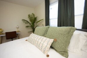 Een hotelkamer met een bed, een bureau, een stoel, een potplant en een raam met gordijnen.