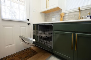Een keuken met een vaatwasser, een spoelbak en een raam met jaloezieën.