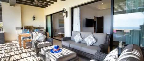 Amplia sala de estar con muebles de mimbre, un sofá gris y un gran ventanal corredero que da a un balcón.