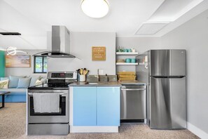 Una cocina compacta con horno empotrado, refrigerador de acero inoxidable y un letrero en la pared.
