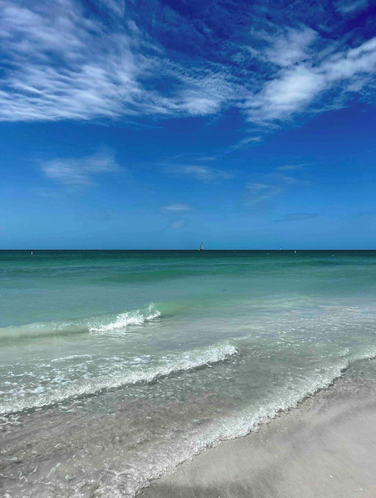 A beach with clear water and a distant boat.