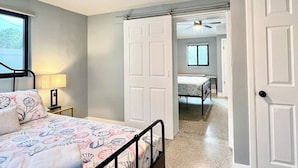 A bedroom with a bed, a nightstand, a lamp, and a door leading to another room.