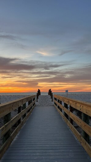 A wooden pier leading to a beach with a sunset in the background.