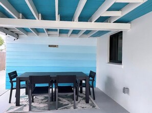 Un patio cubierto con una mesa y sillas, una pared azul y una ventana.