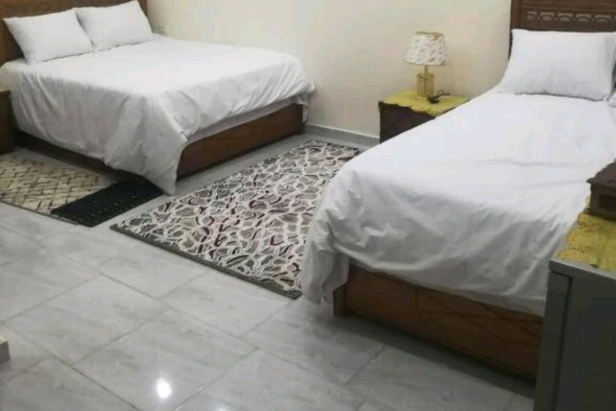 A hotel room with two beds, a patterned rug, and a nightstand with a lamp.