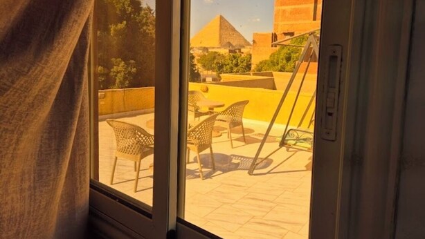 Vista desde una ventana sobre un patio con mobiliario exterior y una estructura piramidal.