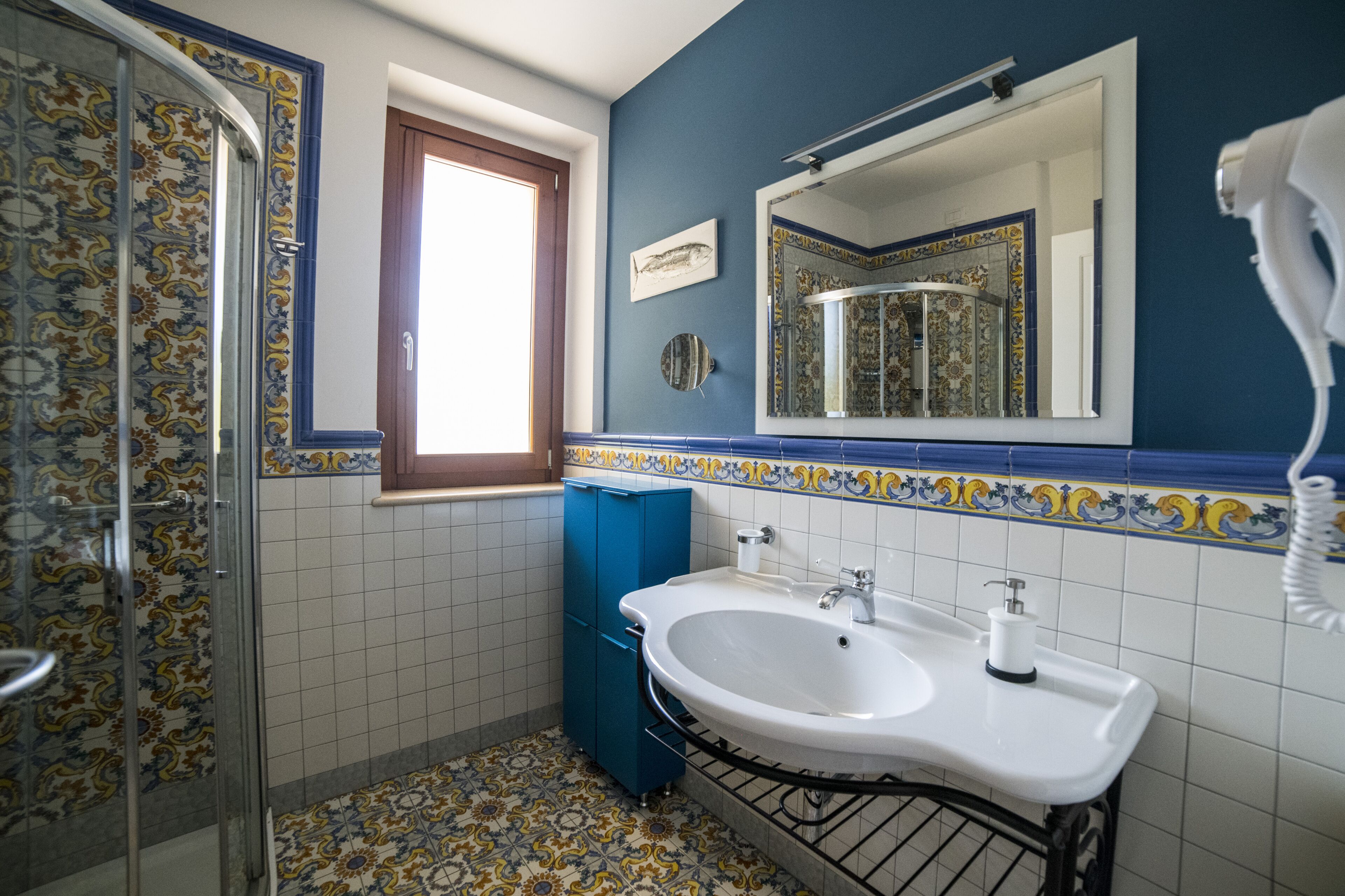 A bathroom with a white sink, blue cabinet, and patterned tiles.