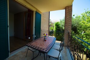 A balcony with a table and chairs, a vase with flowers, and a view of greenery and buildings.