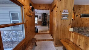 Interior de uma cabana de madeira com lareira de pedra, um banco e um sofá.