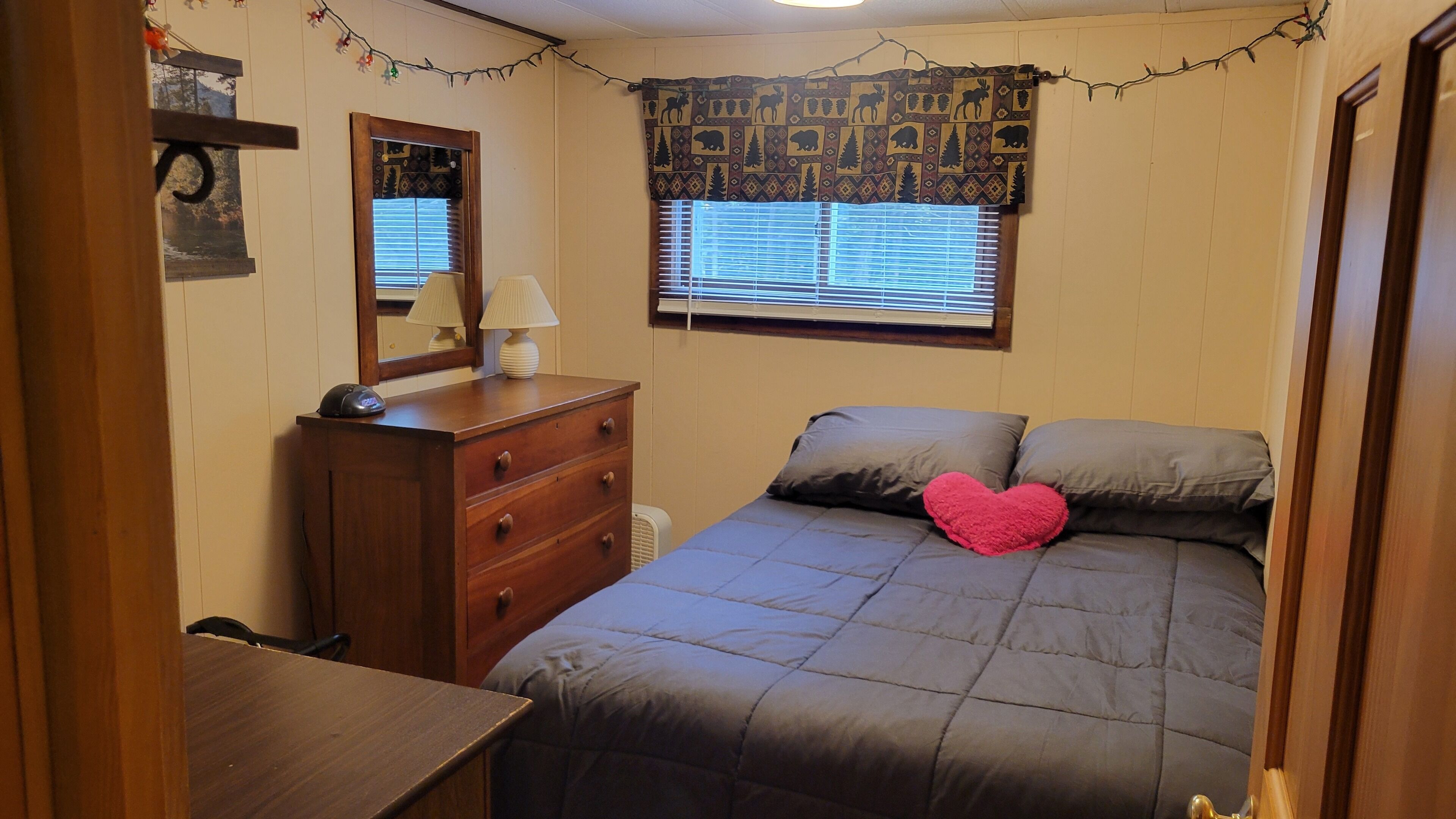 Une chambre à coucher avec un lit, une commode, une lampe et une fenêtre avec des stores.