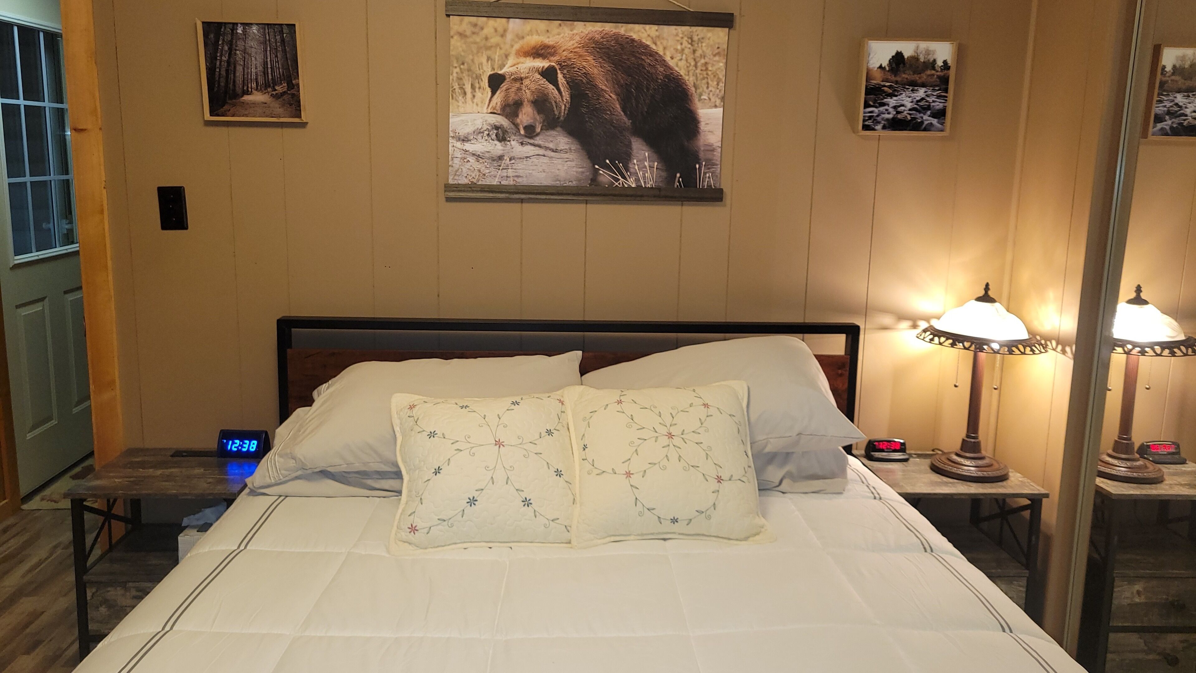 Una habitación de hotel con cama, dos mesitas de noche, un reloj digital y cuadros en la pared.