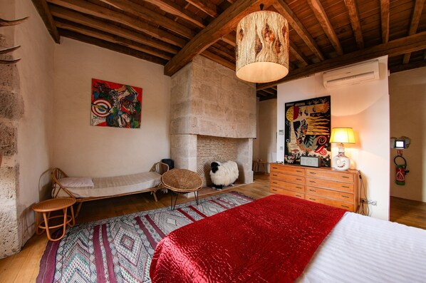 A rustic room with a bed, a fireplace, a wooden dresser, and a hanging light fixture.