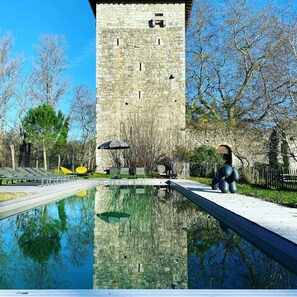 A stone tower with a pool in front, surrounded by trees and outdoor seating.