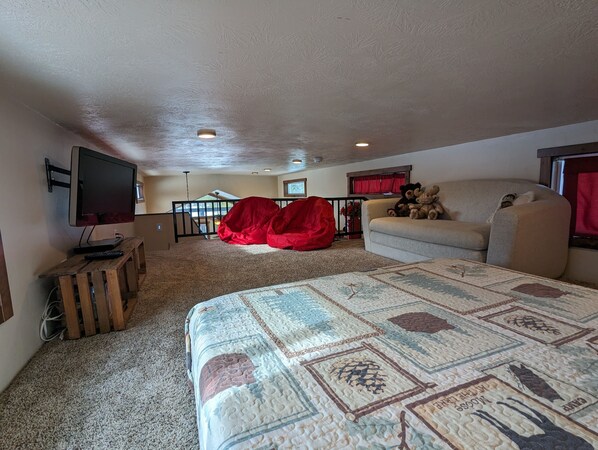 Una sala de estar acogedora con una cama grande, un televisor, un sillón de peluche rojo y un sofá con peluches.