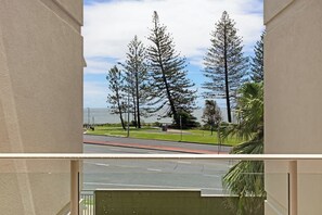 A view from a balcony overlooking a road with trees and a body of water. - Bellardoo 12 Beach View Mooloolaba (Mooloolaba)