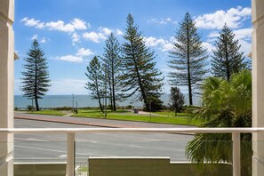 Un balcon donnant sur une route, des arbres et l’océan.