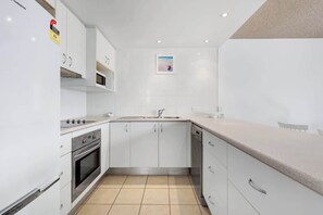 A modern kitchen with white cabinets, a stainless steel oven, and a dishwasher. - Bellardoo 12 Beach View Mooloolaba (Mooloolaba)
