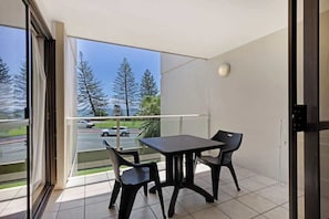 A balcony with a table and chairs, a view of trees and a road, and a door leading to the interior. - Bellardoo 12 Beach View Mooloolaba (Mooloolaba)