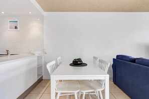 Une cuisine moderne avec des meubles blancs, une table à manger avec quatre chaises, un canapé bleu et une petite plante en pot posée sur la table.