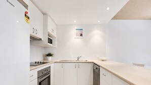 A modern kitchen with white cabinets, a stainless steel range, a dishwasher, and a beige countertop. - Bellardoo 12 Beach View Mooloolaba (Mooloolaba)