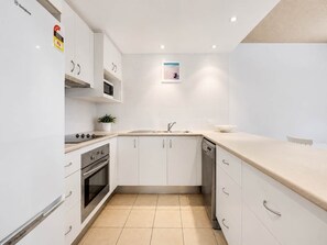 A modern kitchen with white cabinets, a stainless steel range, a dishwasher, and a beige countertop.