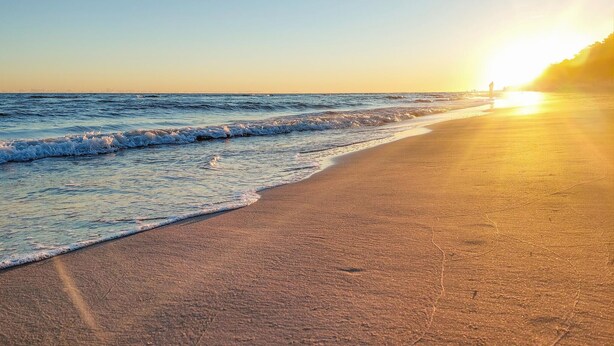 A beach with waves gently lapping at the shore and a sunset in the background. - Beach front home in Rewal with WiFi (Rewal)