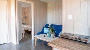 A compact living space with a kitchenette, a blue sofa, a small dining table, and a bed in the background. - Beach front home in Rewal with WiFi (Rewal)