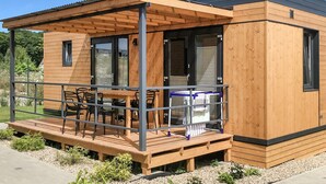 A modern wooden cabin with a covered patio area, featuring a table and chairs, and large windows. - Beach front home in Rewal with WiFi (Rewal)