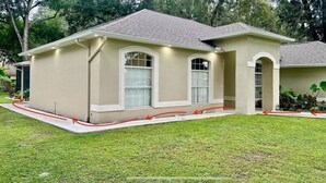 A single-story house with a beige exterior, large windows, and a covered porch area. - Charming , 2 bedroom , 1 bath  (Kissimmee)