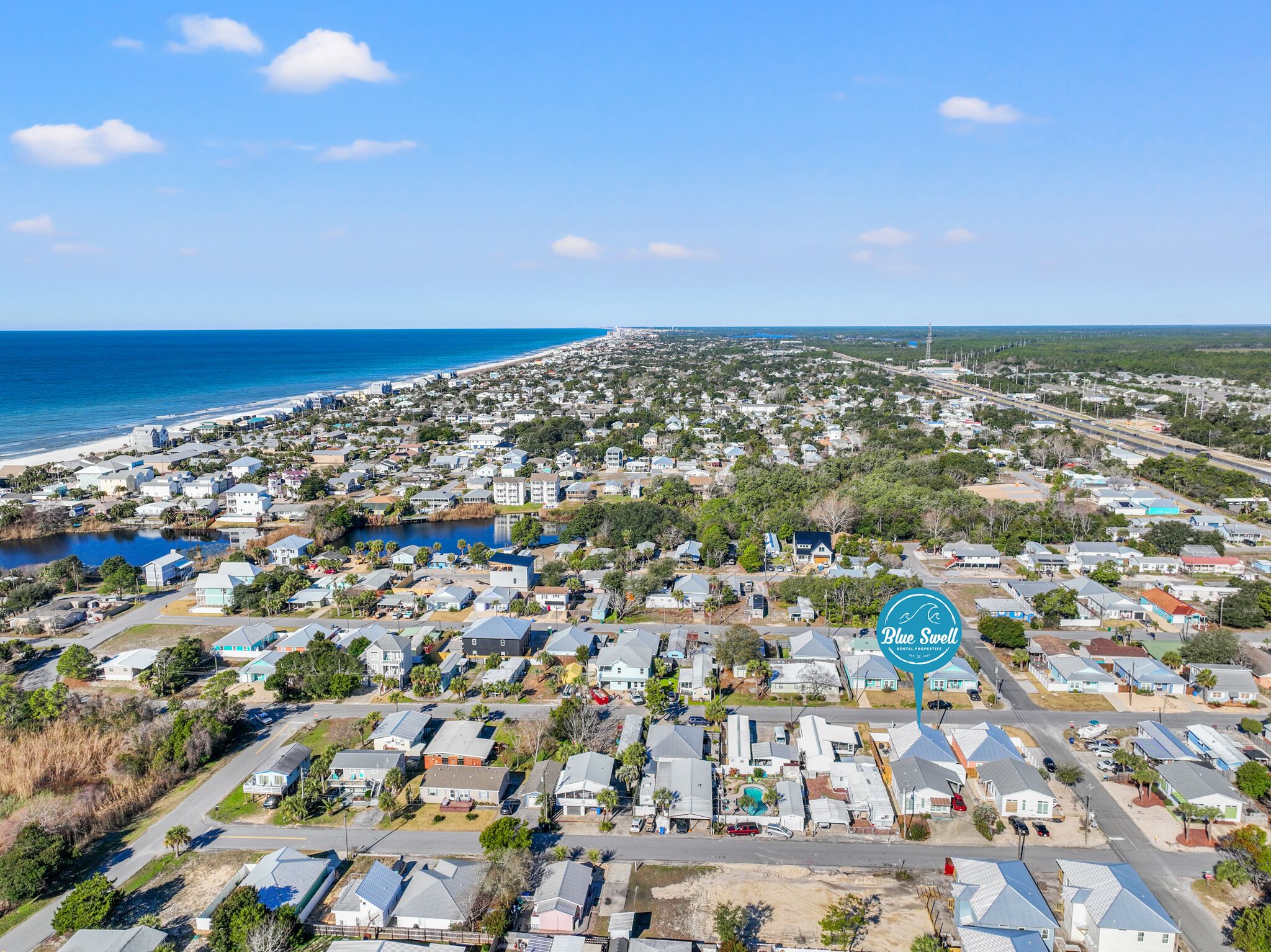 Vista aérea de uma área residencial costeira com casas, uma praia e um corpo de água.