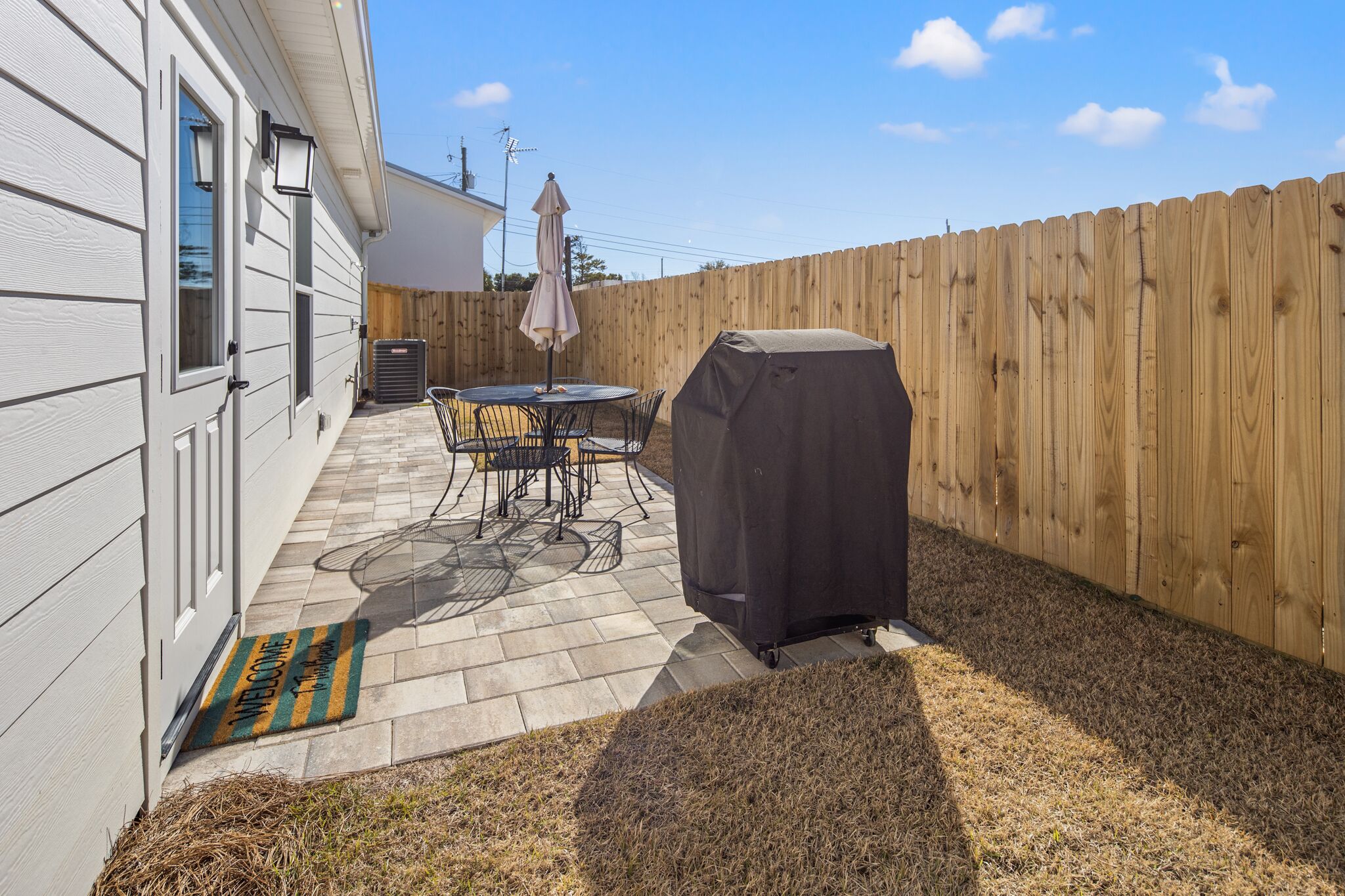 A backyard with a patio, a covered grill, a table with chairs, and a wooden fence.