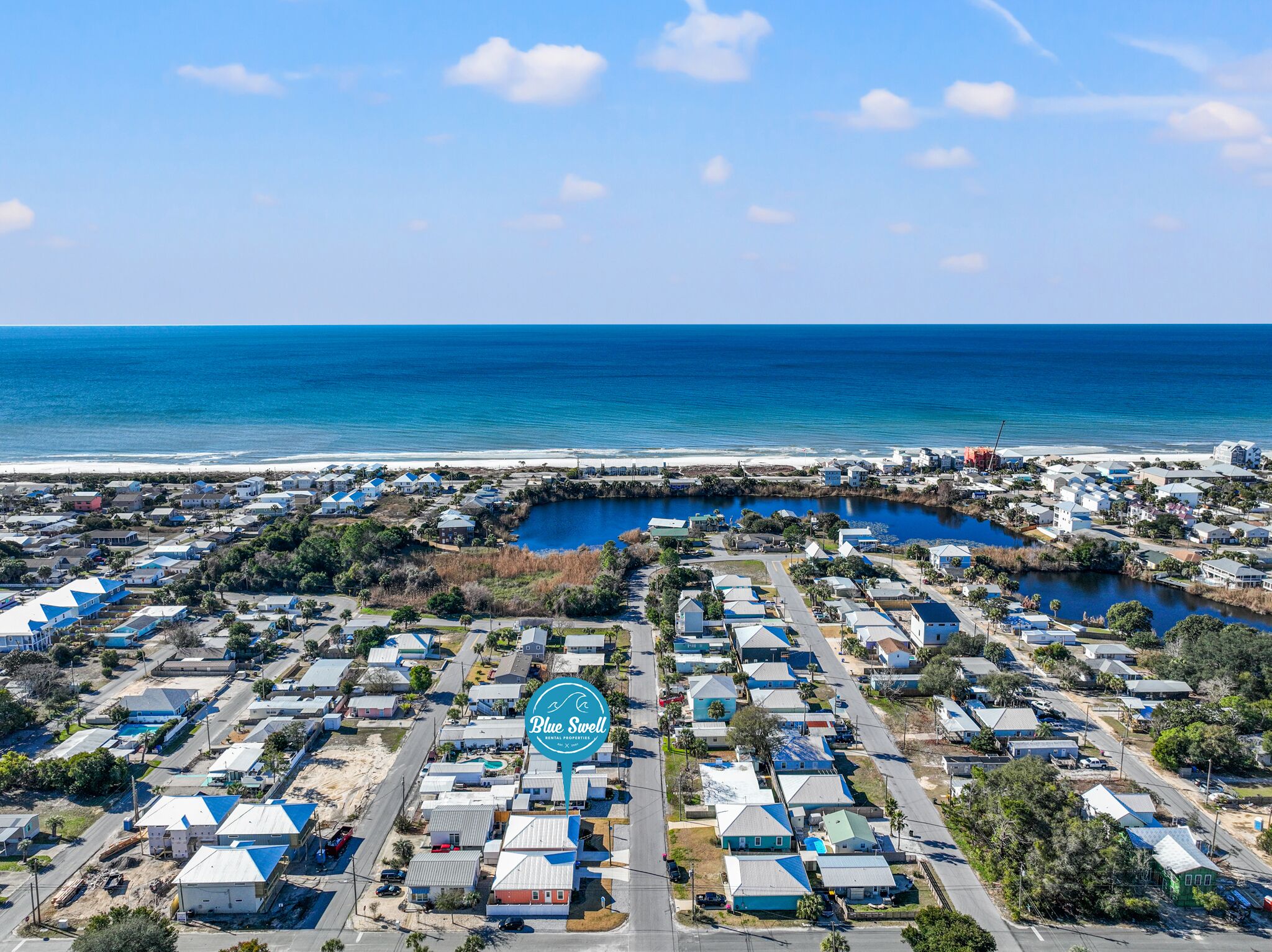 An aerial view of a coastal residential area with a marina, houses, and a beach.
