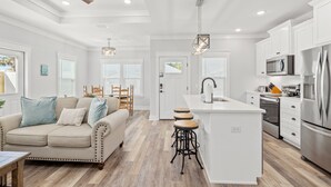 A modern kitchen with white cabinetry, a central island with stools, and stainless steel appliances. - Laguna Haven! 3BR 2BA Sleeps 7! Your Perfect Escape! (Panama City Beach)